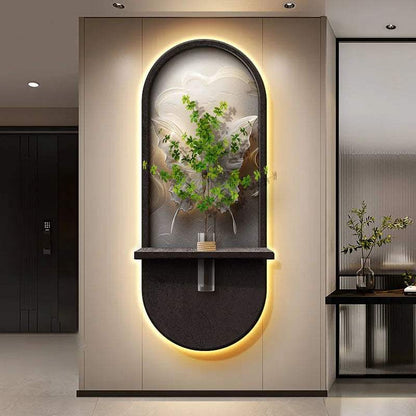 Green Plant Wall Lamp with an illuminated oval black frame, arched relief panel, and central shelf holding a leafy plant